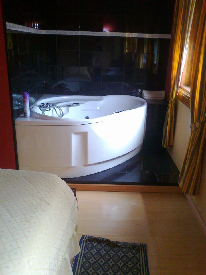 Uma banheira de hidromassagem branca em um banheiro com azulejos pretos, ao lado de uma cama .