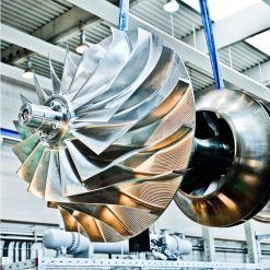 Große, glänzende Turbinenbauteile hängen in einer Fabrikhalle.