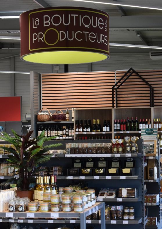 Intérieur rustique d'une boutique avec des étagères remplies de bocaux, de bouteilles et de produits emballés, disposées sur des tables en bois et des murs en pierre.