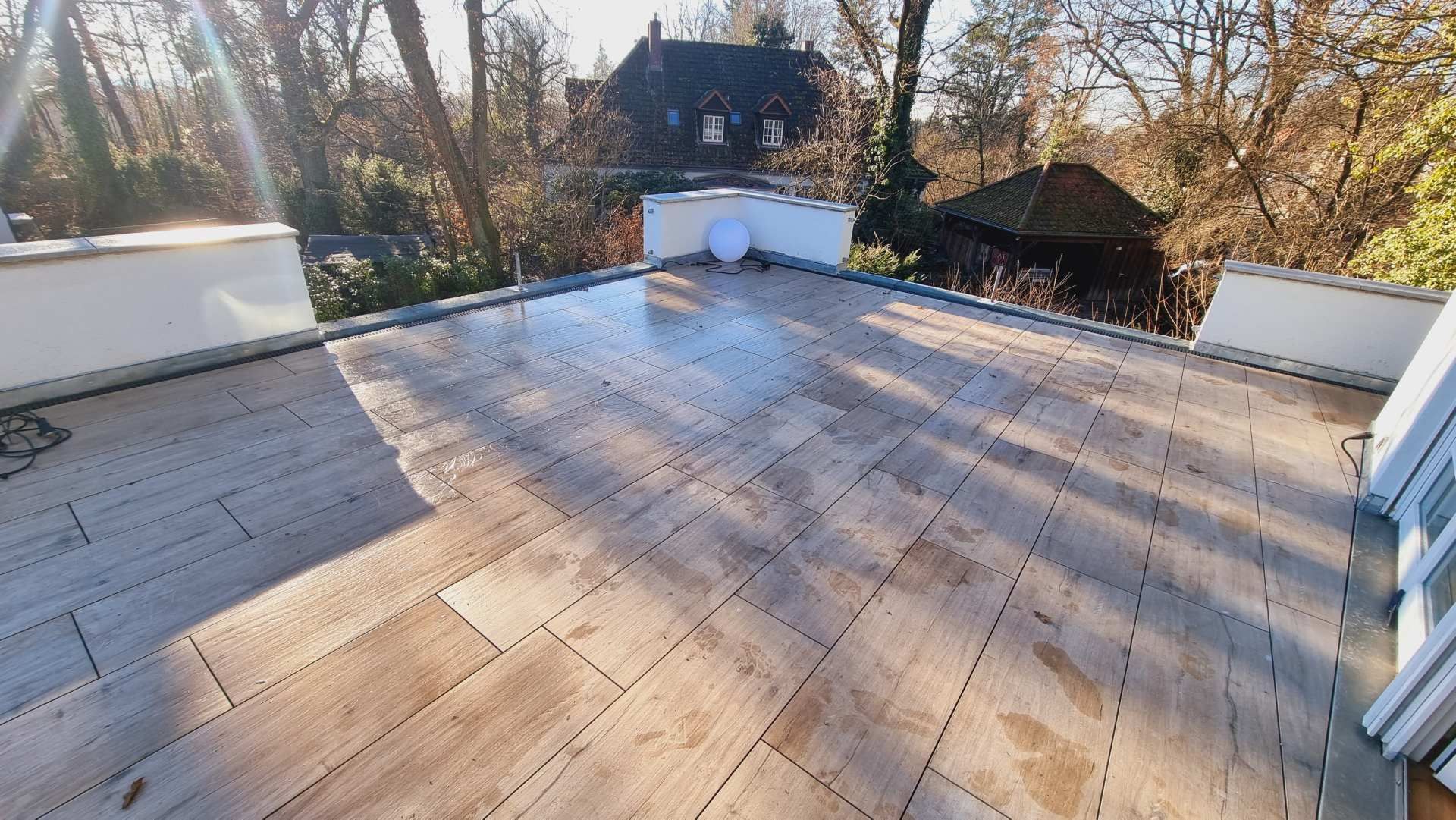 Dachterrasse mit hellen Holzplanken und weißem Geländer mit Blick auf Bäume und Nachbarhäuser