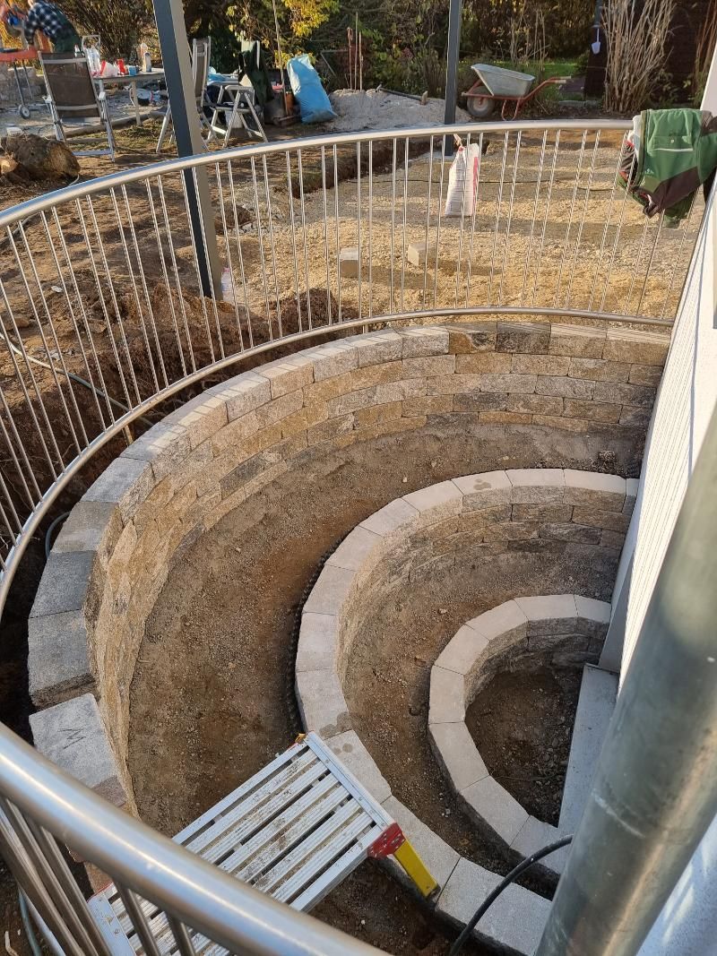 Geschwungenes Steintreppenhaus, das unterirdisch hinabführt, mit Metallgeländer und einer Baustelleneinrichtung darüber.