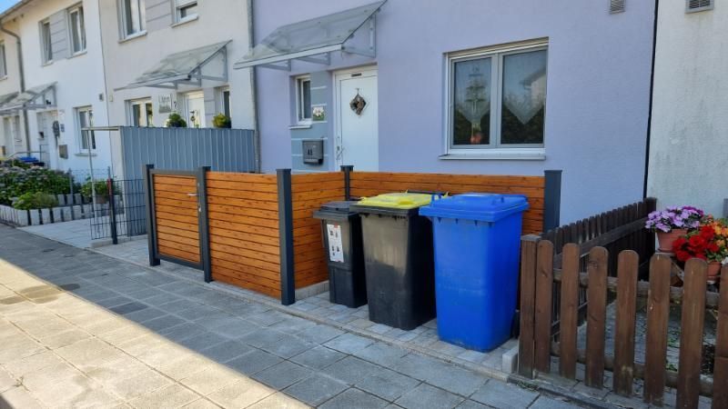 Eine Häuserreihe mit Mülltonnen am Bürgersteig und hölzernen Sichtschutzzäunen in einer Wohnstraße