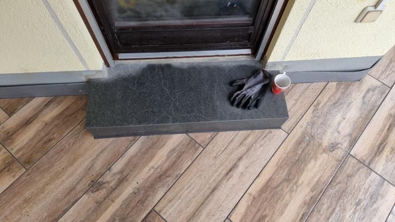 Fußmatte vor der Haustür, schwarze Handschuhe und eine rote Dose auf einer hölzernen Verandastufe