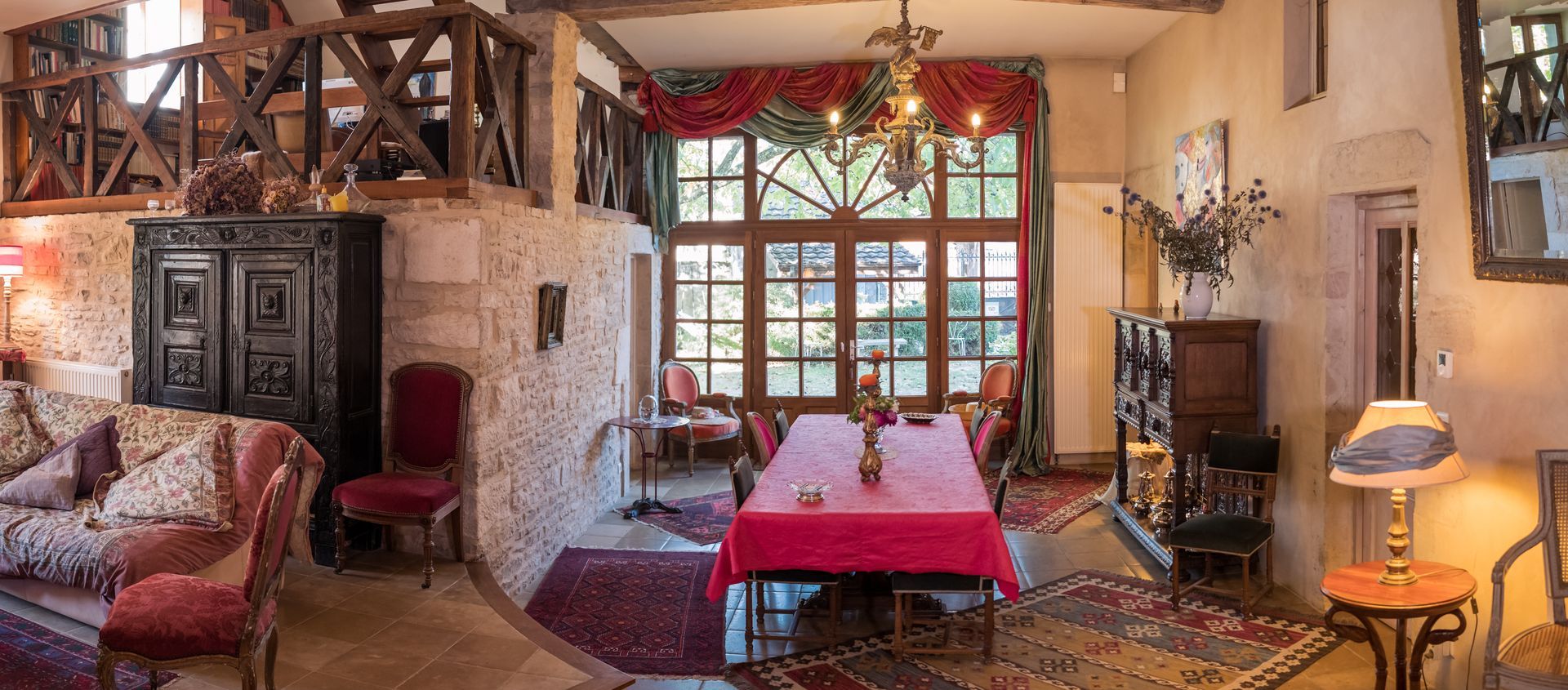Une salle à manger chaleureuse avec une nappe rouge, un lustre et une grande fenêtre.