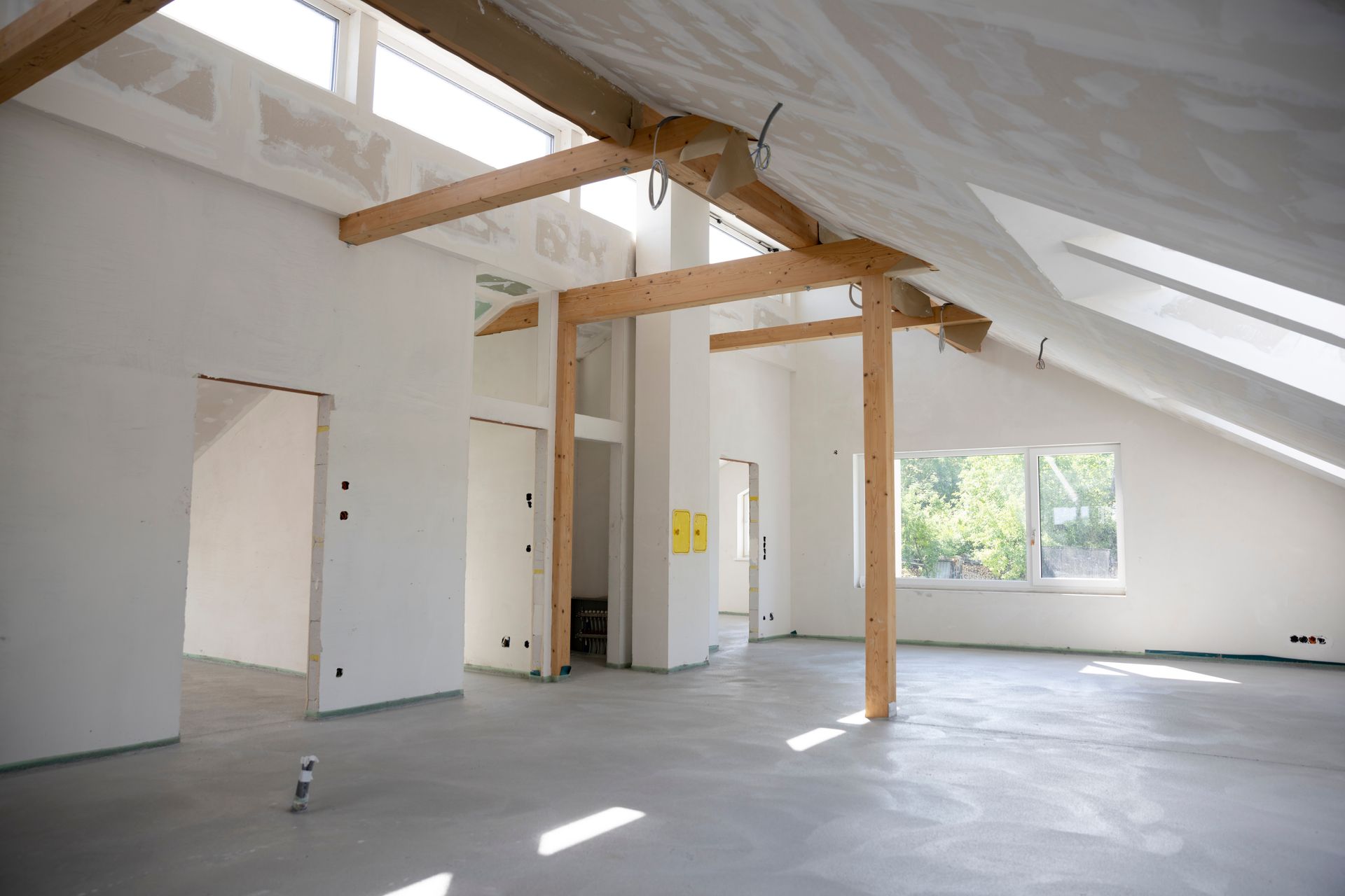 Intérieur d'une pièce en construction avec murs blancs, poutres en bois apparentes et sol en béton.