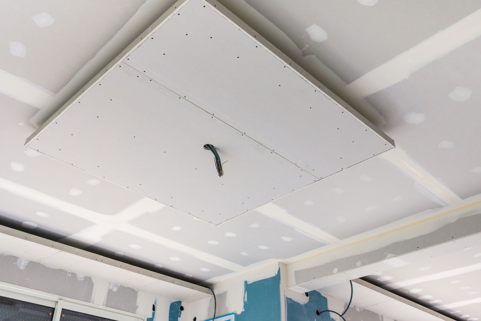 Plafond en plaques de plâtre avec une section carrée en retrait, non fini, dans une pièce en construction.