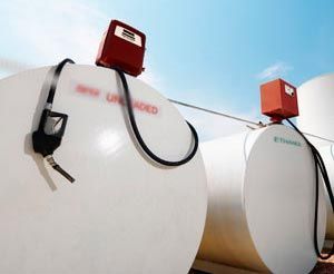 Depósitos de combustible con surtidores rojos acoplados y mangueras negras, contra un cielo azul.