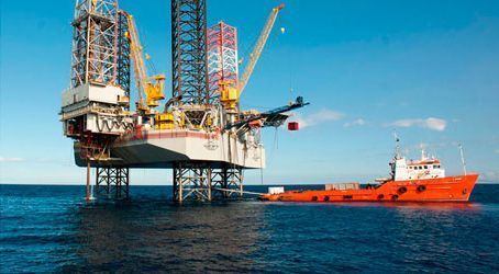 Plataforma petrolífera marina con buque de apoyo en un mar azul bajo un cielo despejado.