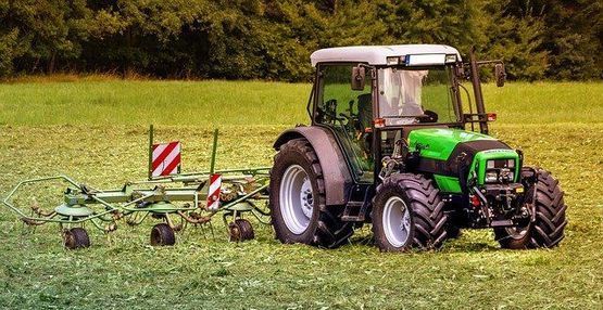 Tractor verde con rastrillo acoplado trabajando en un campo de hierba verde.