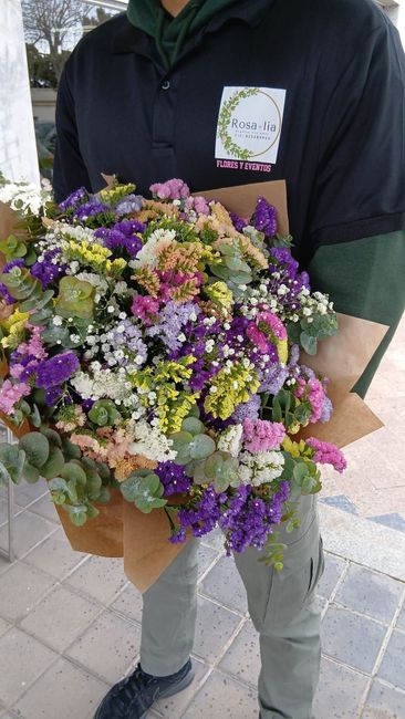 Persona sosteniendo un gran ramo colorido de flores silvestres envuelto en papel marrón.