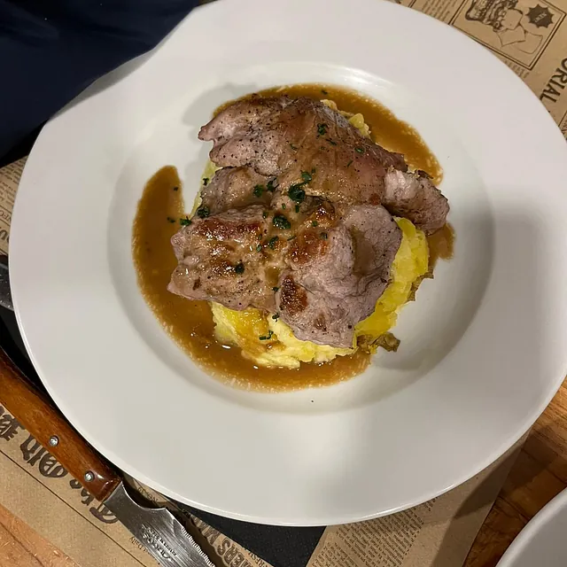 Un plato blanco cubierto con carne y puré de papas.