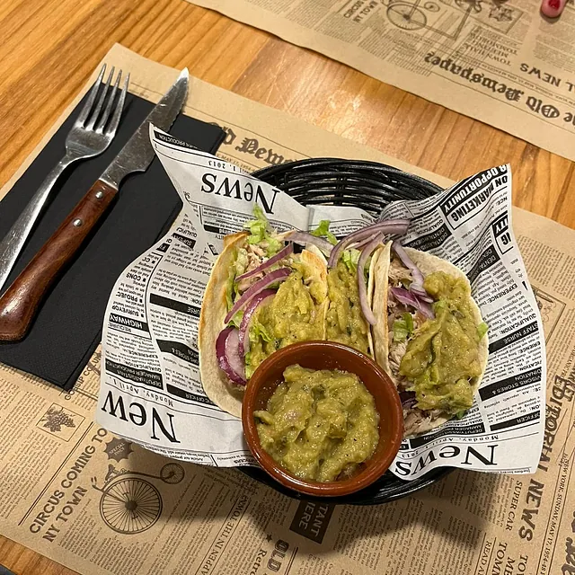 Un plato de comida con un bol de guacamole sobre papel de periódico.