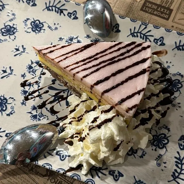 Una rebanada de pastel en un plato con crema batida y salsa de chocolate.