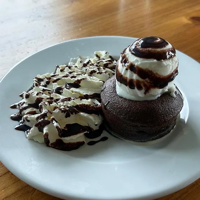 Un pastel de chocolate con crema batida y salsa de chocolate en un plato blanco.