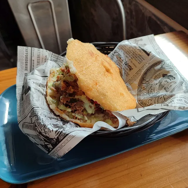 Un sándwich envuelto en papel de periódico reposa sobre una bandeja azul.