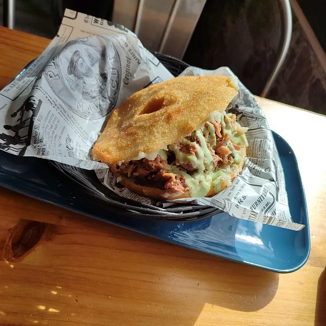 Un sándwich envuelto en papel de periódico reposa sobre una bandeja azul.