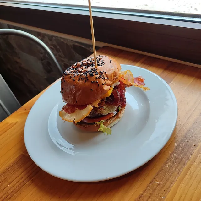 Una hamburguesa en un plato blanco con un palillo sobresaliendo de ella.