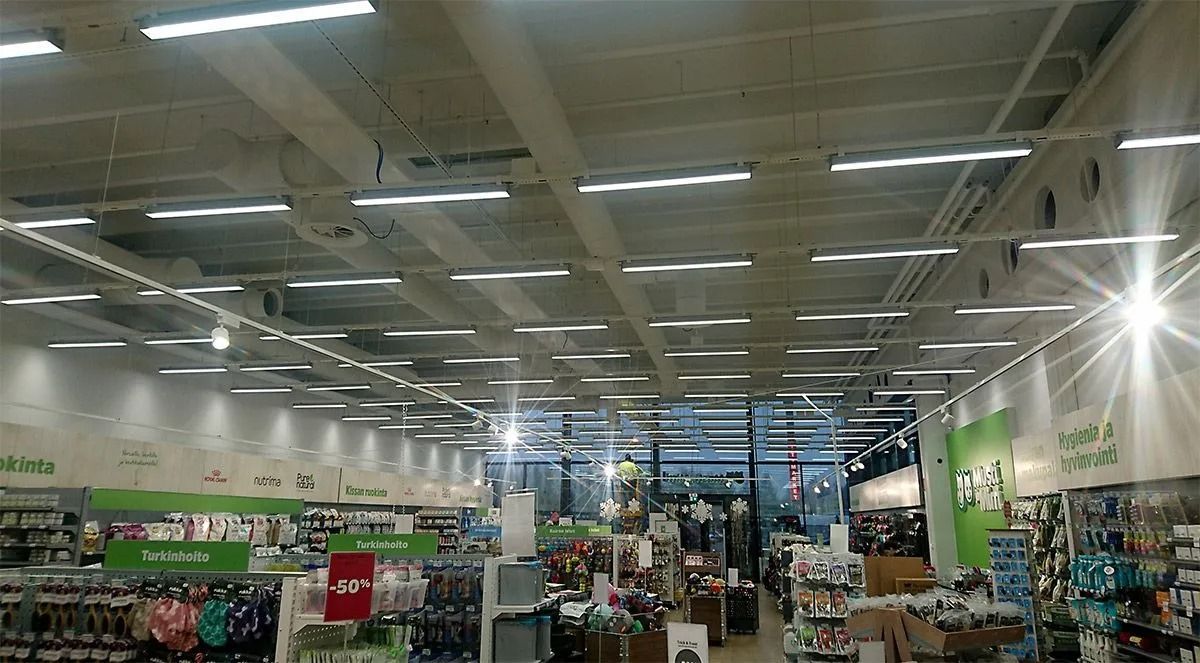 Sisäkuva kirkkaasta vähittäismyymälästä, jossa on pitkiä rivejä loisteputkivalaisimia valkoisessa teollisuuskatossa.