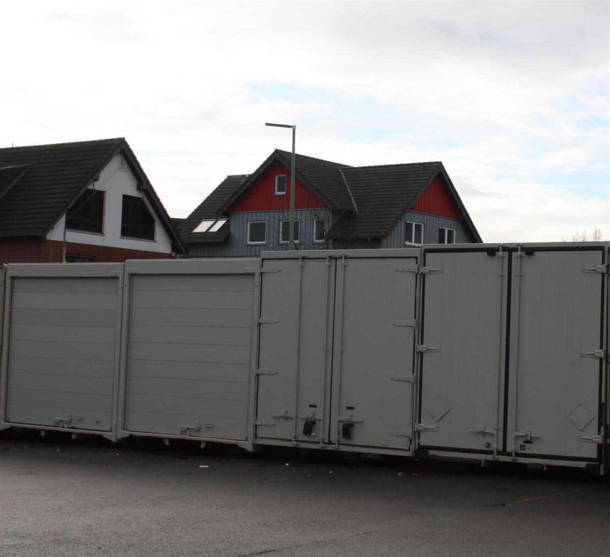 Eine Reihe weißer Container steht vor einem Haus mit rotem Dach