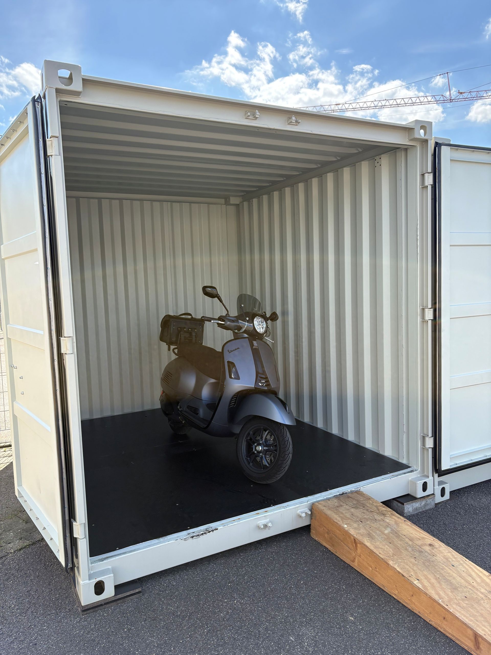 Ein Roller steht in einem offenen weißen Schiffscontainer auf einem gepflasterten Parkplatz.