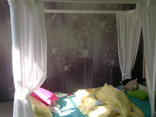 Ein Bett mit Baldachin und einem Bild von Löwenzahn an der Wand