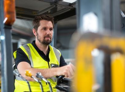 Ein Mann in einer gelben Weste fährt einen Gabelstapler in einer Fabrik.