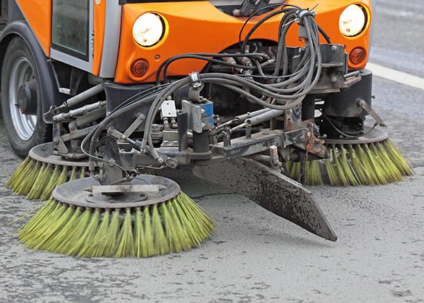 Eine orangefarbene Straßenkehrmaschine reinigt die Straße mit grünen Bürsten