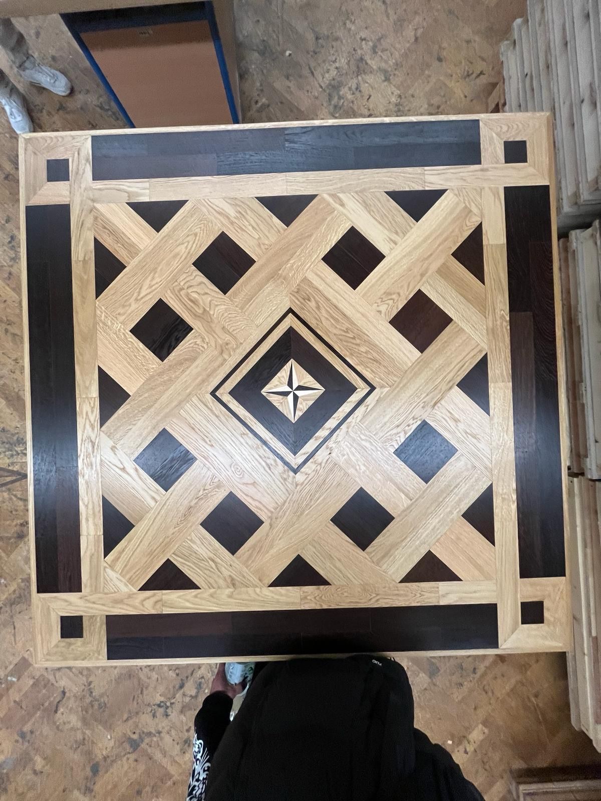 Quadratische Holztischplatte mit geometrischem Muster aus hellem und dunklem Holz.