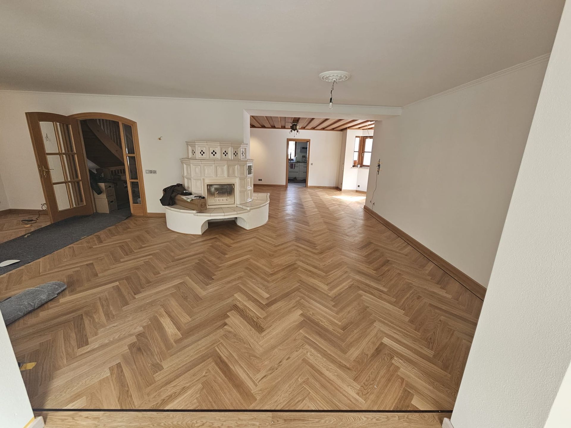 Lichtdurchflutetes Wohnzimmer mit Fischgrätholzböden, Kamin und Tür zu einem anderen Zimmer.