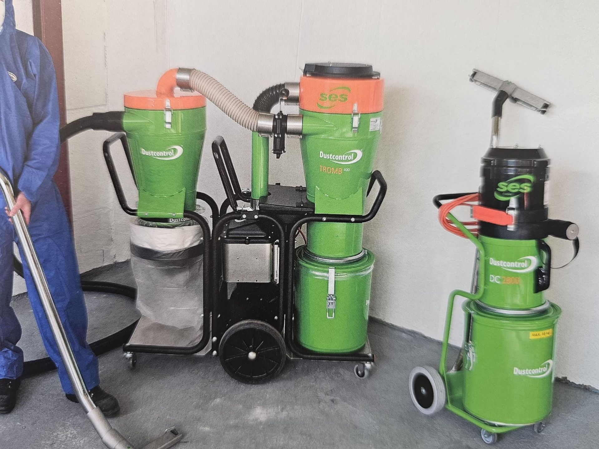Drei grüne Werkstattsauger, aufgereiht mit Schläuchen und Rädern in einer Garage oder Werkstatt.