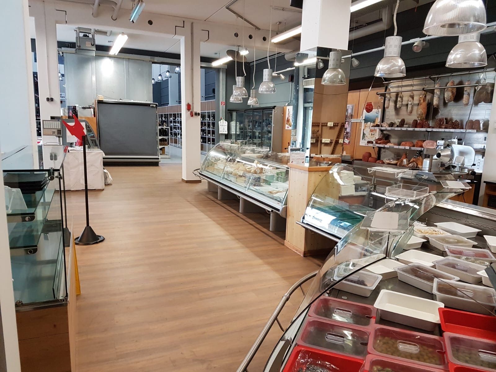 Innenansicht eines Lebensmittelmarktes; Vitrinen mit verschiedenen Lebensmitteln, Holzboden, helle Beleuchtung.