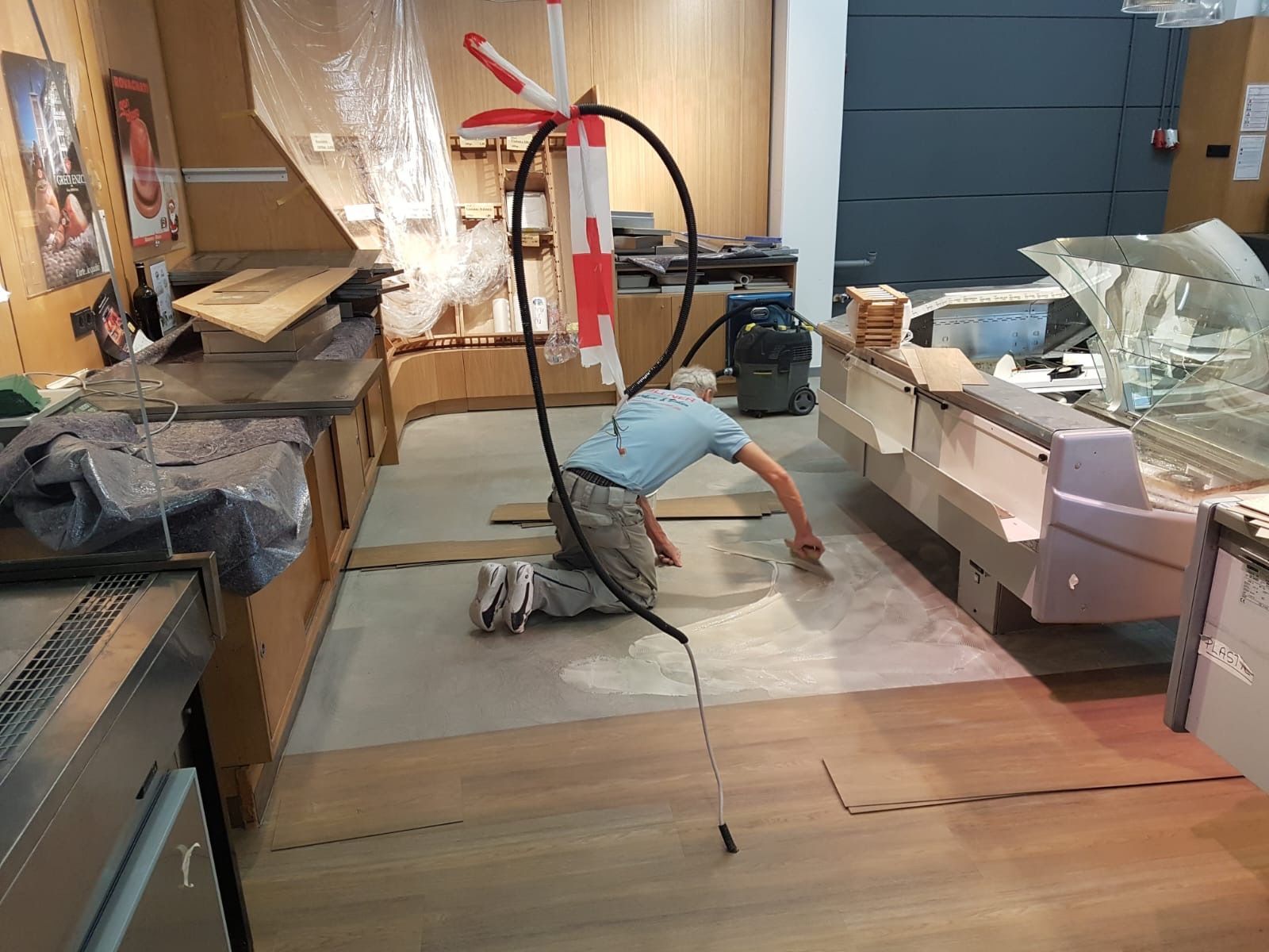 Person, die in einer Großküche in der Nähe von Theken und Geräten einen Bodenbelag verlegt.