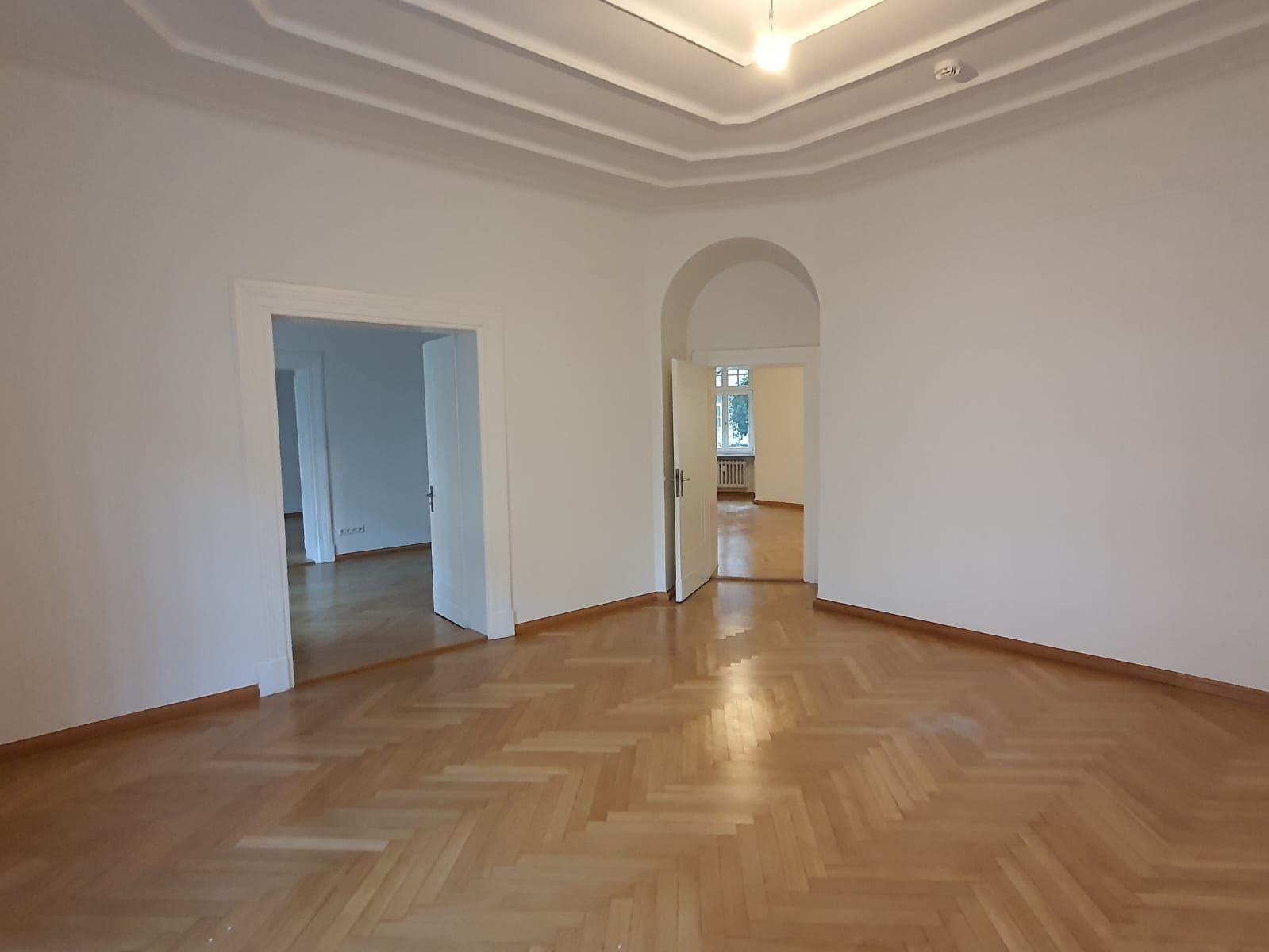 Leerer Raum mit Hartholzböden, gewölbter Tür und dekorativer Decke.