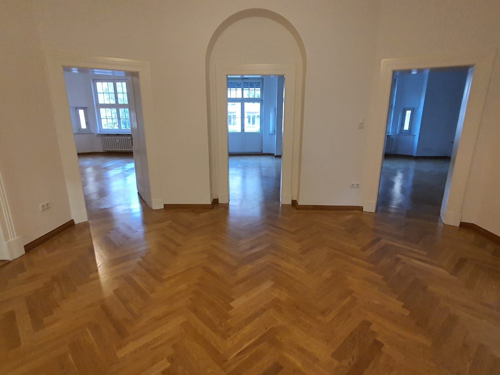 Leerer Raum mit Parkettboden und drei Türen zu anderen Räumen, Tageslicht.