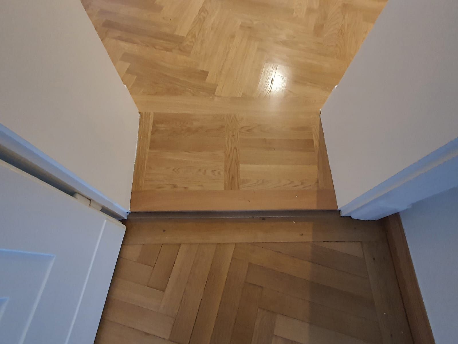 Fischgrätboden aus Holz in einem Türrahmen mit weißen Wänden und Türrahmen.