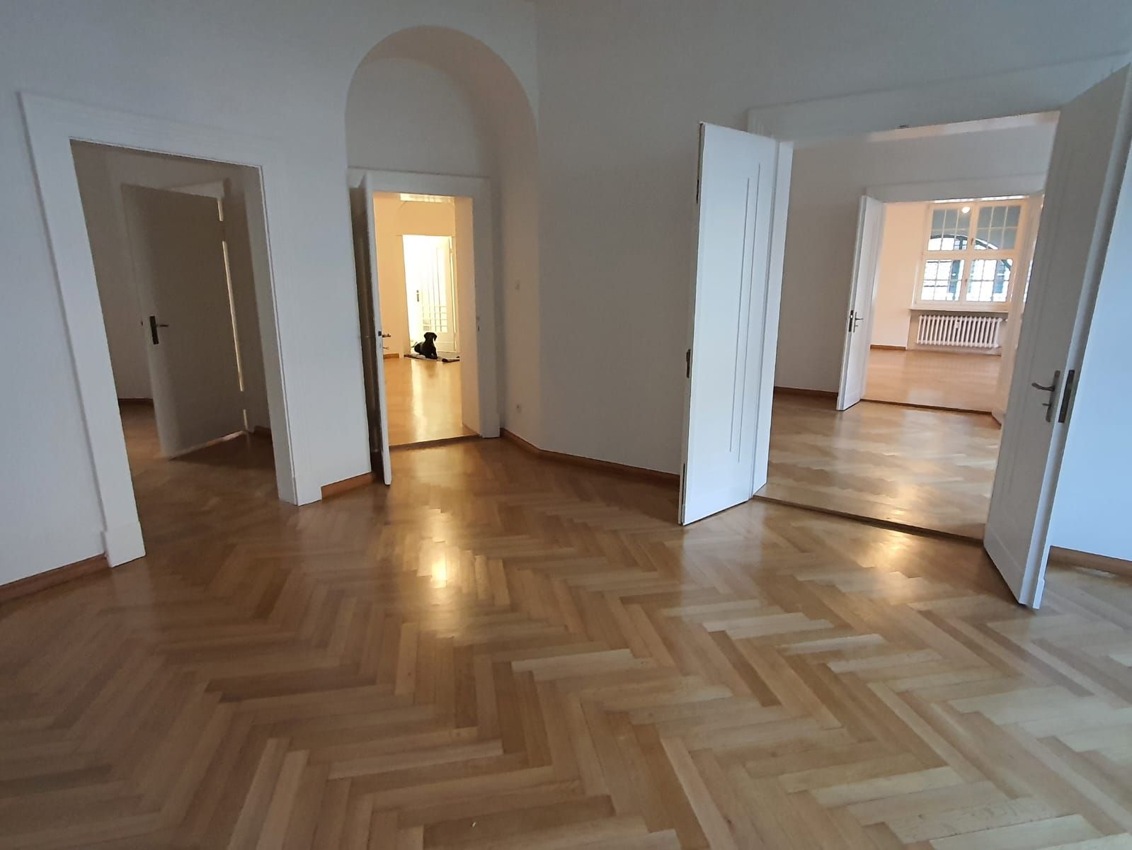 Leerer Raum mit Parkettboden, weißen Wänden und offenen Türen.