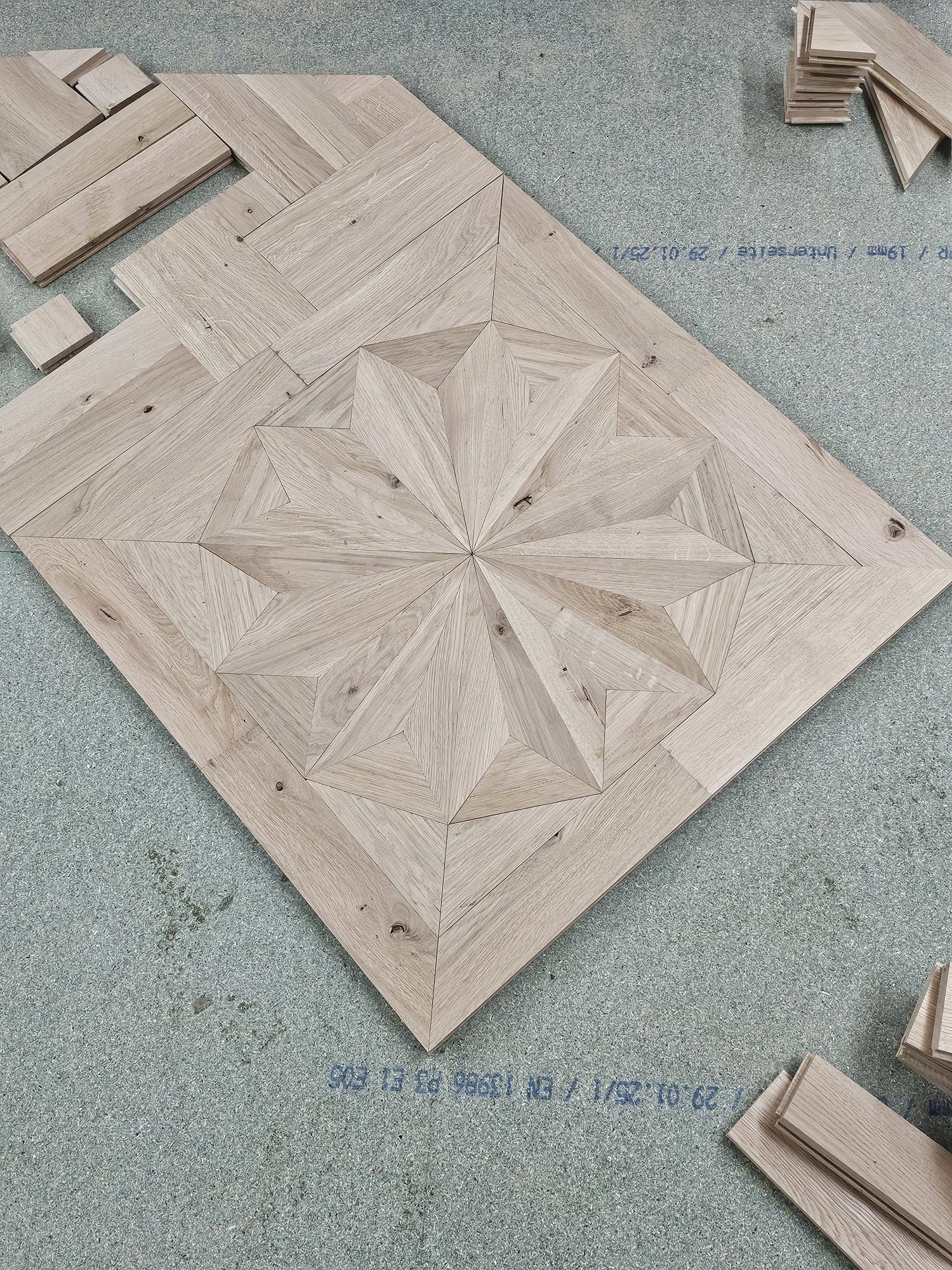 Holzparkettboden mit Sternenmuster, teilweise montiert auf einer gesprenkelten, blaugrauen Oberfläche.