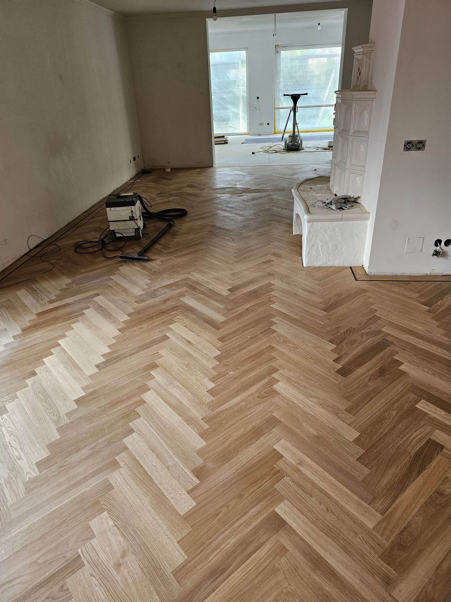 Fischgrät-Holzboden in einem Raum, mit Werkzeugen und einem Kamin im Hintergrund.