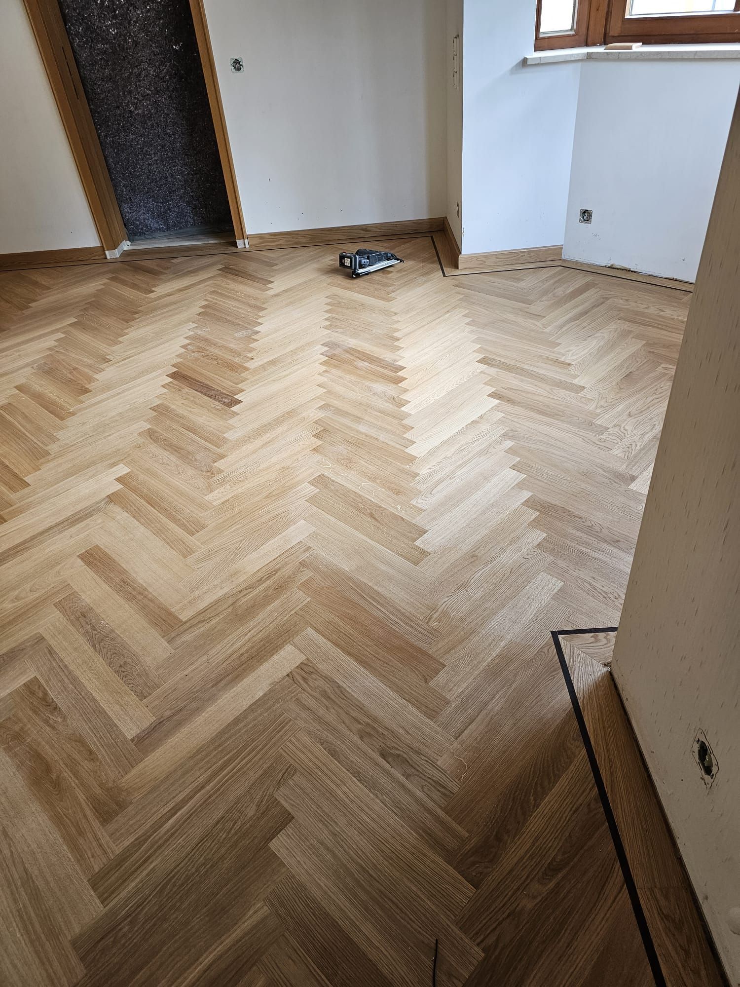 Holzboden mit Fischgrätenmuster in einem Raum, neben einer Tür und einer Wand.