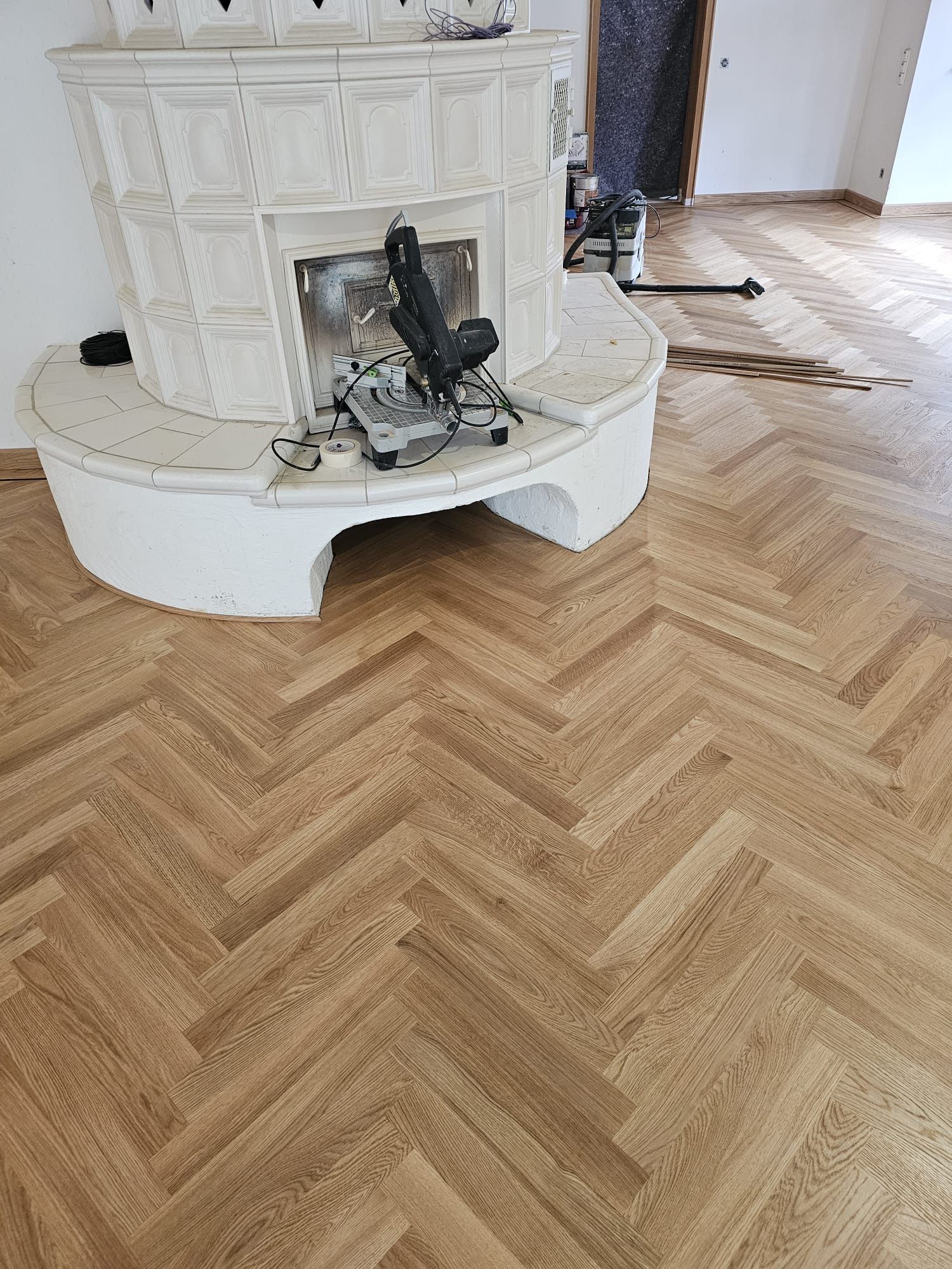 Fischgrät-Holzboden mit weiß gefliestem Kamin.