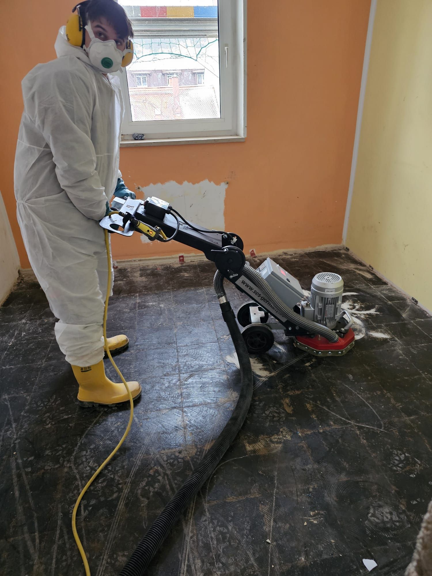 Ein Mann im Schutzanzug reinigt mit einer Maschine einen Boden.