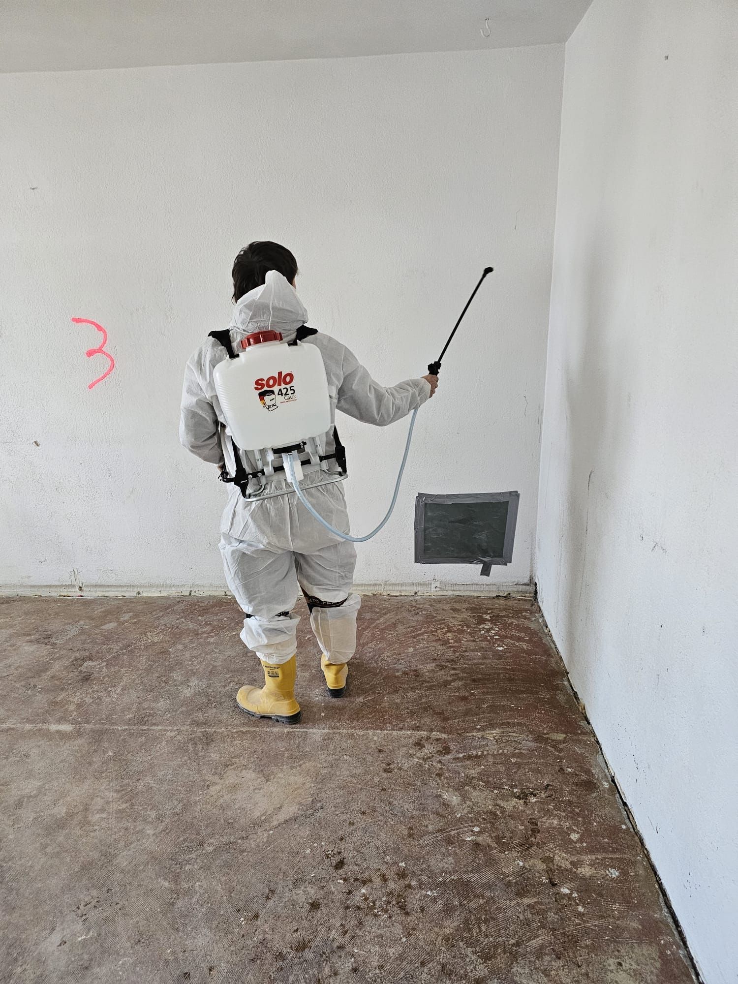 Ein Mann im Schutzanzug besprüht eine Wand mit einer Sprühpistole.