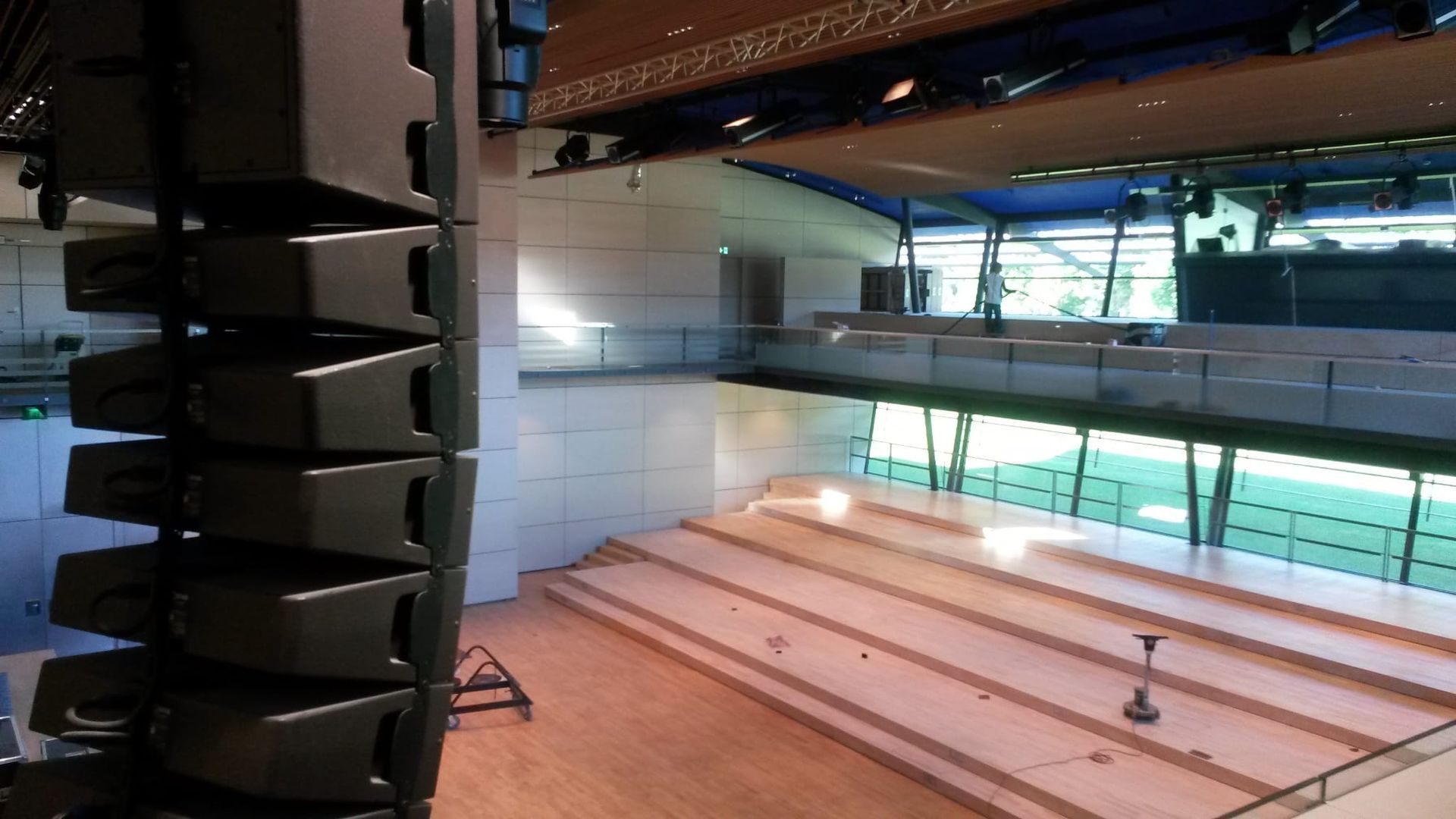 Eine Reihe von Lautsprechern hängt in einem modernen Auditorium mit Bühne, Sitzgelegenheiten und Fenstern.