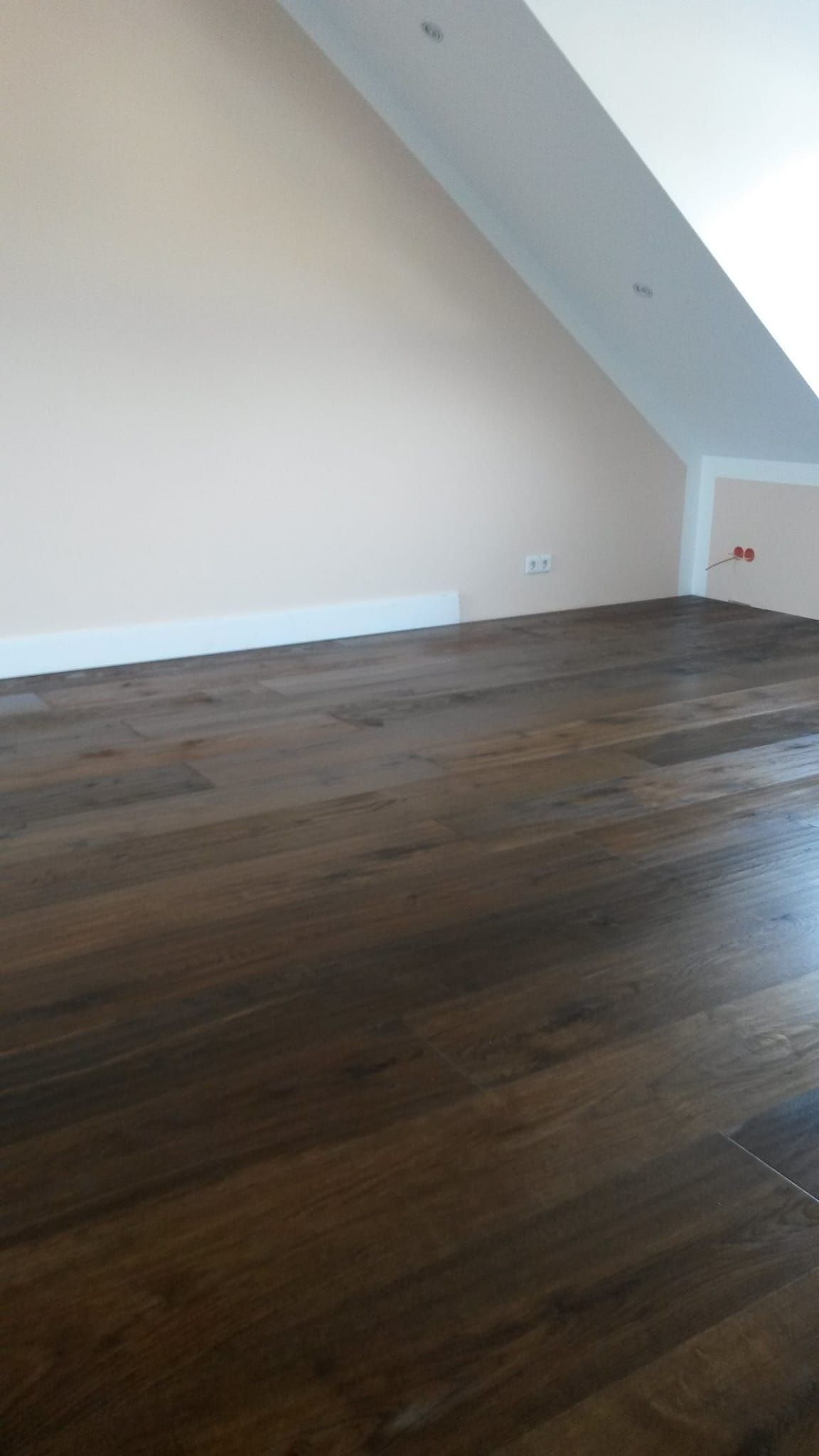 Dunkler Holzboden in einem Dachzimmer mit schräger Decke und blassrosa Wänden.