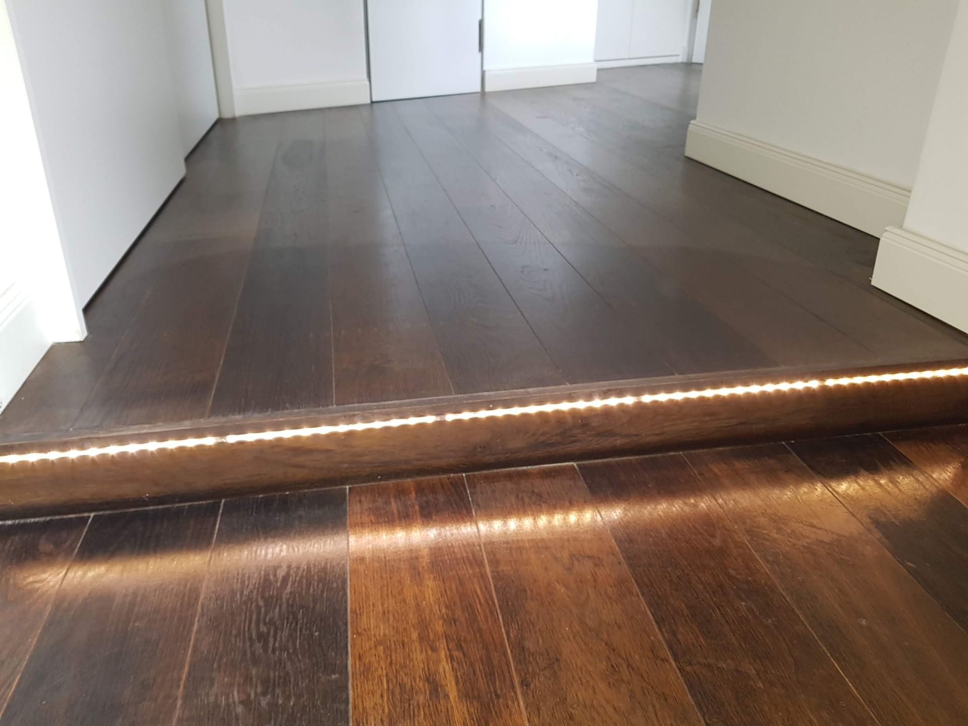 Dunkler Holzboden mit eingelassener warmer LED-Streifenbeleuchtung.