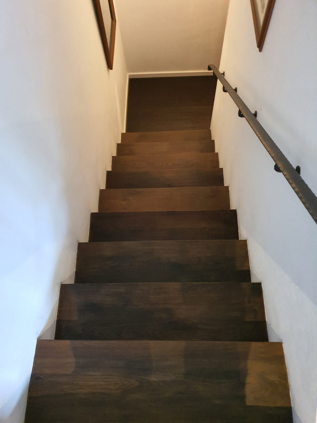 Dunkle Holztreppe mit Metallgeländer an einer weißen Wand.