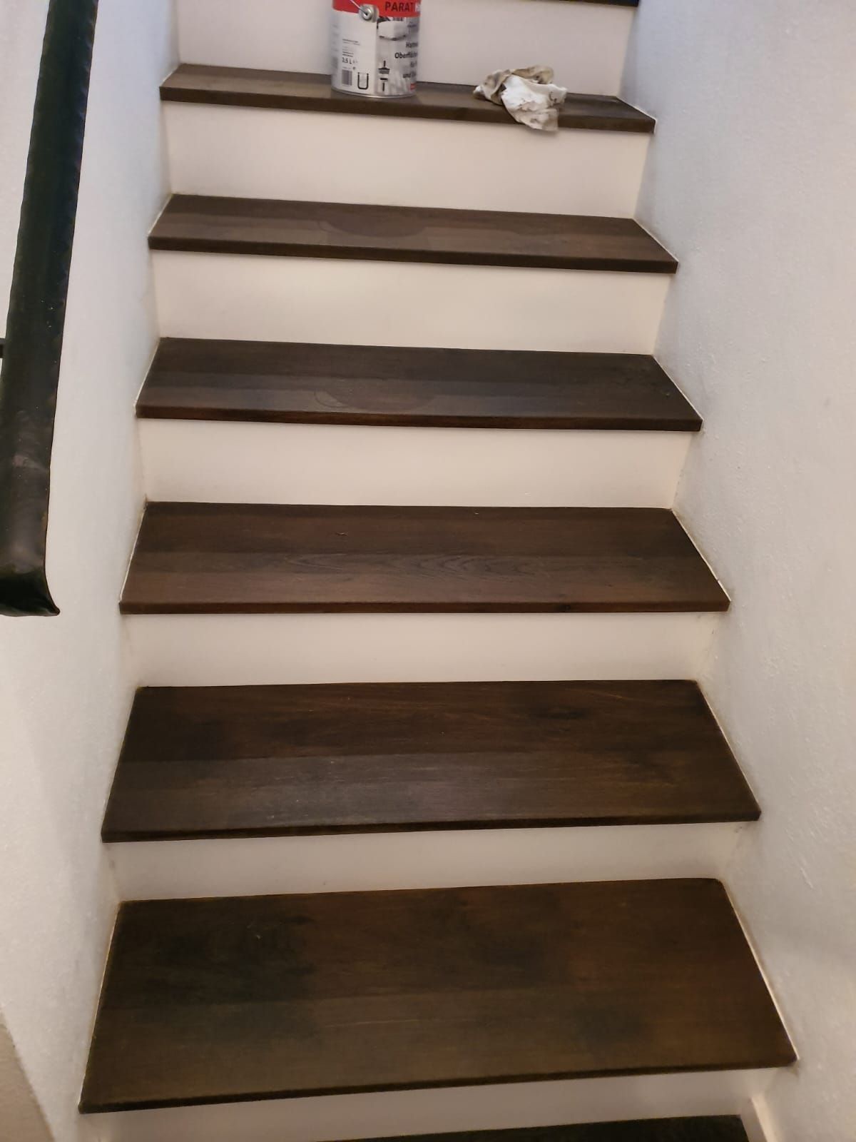 Dunkle Holztreppe mit weißen Setzstufen, die nach oben führt.