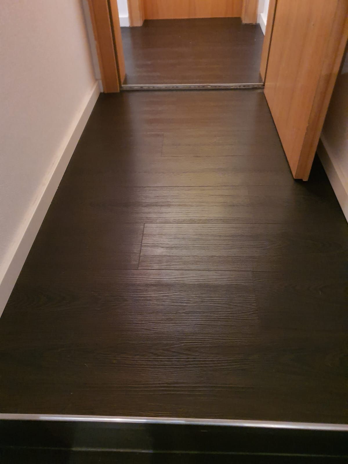 Dunkler Boden in Holzoptik im Flur, weiße Wand links und Holztür rechts.