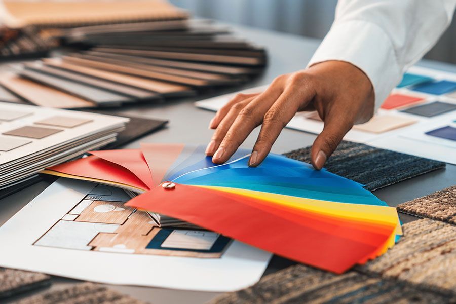 Eine Hand wählt Farbmuster in Blau, Gelb und Rot aus, auf einem Tisch liegen Grundrisse und Stoffmuster.