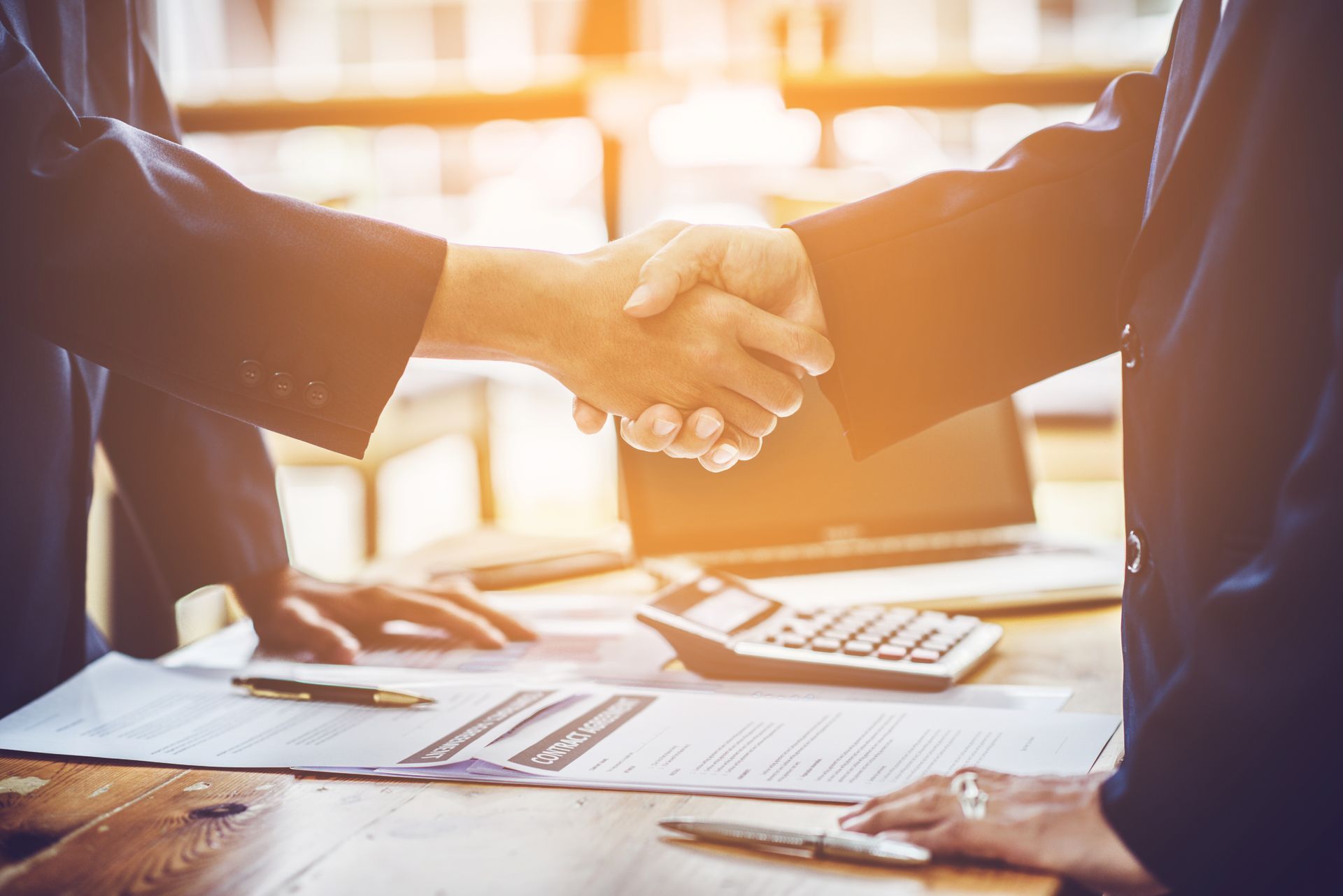 Deux hommes en costume se serrant la main au dessus d'un bureau